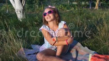 在大自然中野餐。 一个十几岁的女孩坐在村里的草地上晒太阳。 她戴着粉红色的太阳镜，上面有绷带